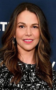 a woman with long brown hair wearing a black and white dress smiling at the camera