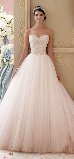 a woman in a wedding dress standing next to a wall with white flowers on it