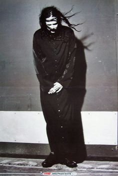 a man with long hair and makeup standing in front of a wall wearing a black outfit