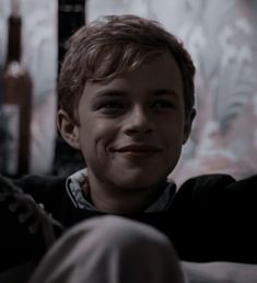 a young boy sitting on top of a couch next to a wall with bottles behind him