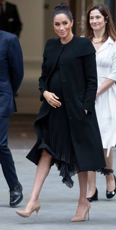 the pregnant woman is walking down the street in her black dress and coat with heels