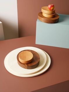 two plates with wooden bowls on them sitting on a table next to an apple in a bowl