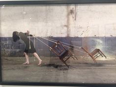 a woman pulling two wooden chairs on strings in an empty room with no one around