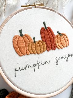 an embroidered hoop with three pumpkins on it and the words pumpkin season written in cursive writing