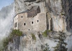 an old castle built into the side of a mountain with fog in the air and birds flying around