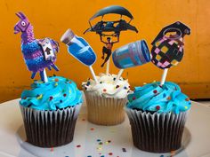 three cupcakes decorated with blue frosting and decorations on top of a white plate