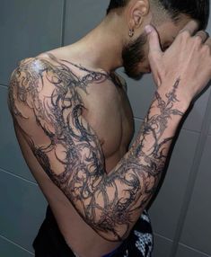 a man with tattoos on his arm and shoulder covering his face in front of a mirror