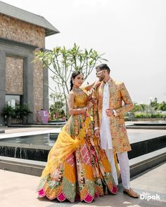 a man and woman standing next to each other in front of a fountain wearing colorful outfits