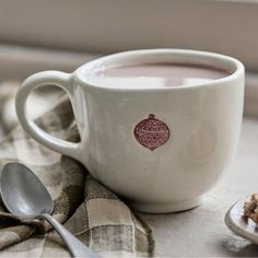 a cup of hot chocolate next to some spoons on a cloth with an ornament