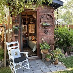 a garden shed with potted plants on the side and a rocking chair in front