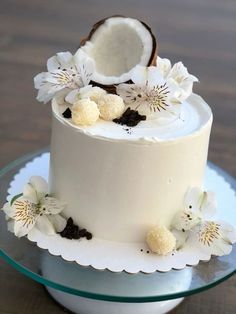 there is a white cake with flowers on the top and coconut in the middle, sitting on a glass plate