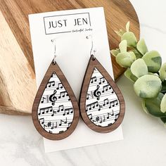 a pair of wooden earrings with musical notes printed on them, sitting next to a plant