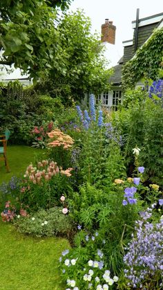 a garden filled with lots of flowers next to a green lawn and wooden chair on the grass