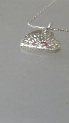 Made to Order: Handmade by Alison and finished by yours truly. Natural ruby (heat treated but not glass filled). Round cut with carat weight of 0.08ct that is bezel set. Lines lead out from ruby like a starburst. Pendant measures approximately 0.57 inches from top to bottom and 0.47 inches wide. Birthstone for July. Made of solid fine silver and comes with 18 inch sterling silver Cardano style chain with lobster clasp. Ruby Heart Pendant Jewelry For Anniversary, Heart-shaped Jewelry With Bezel Setting For Valentine's Day, Heart-shaped Bezel Set Jewelry For Valentine's Day, Anniversary Ruby Jewelry With Heart Charm, Heart-shaped Ruby Birthstone Jewelry, White Gold Heart-shaped Jewelry With Bezel Setting, Anniversary Heart Necklace With Bezel Setting, Silver Heart-shaped Jewelry With Bezel Setting, Silver Sterling Silver Heart Cut Birthstone Necklace