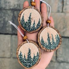 three handmade ornaments with trees on them are hanging from the palm of a person's hand