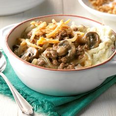 a white bowl filled with mashed potatoes covered in meat and gravy on top of a green napkin