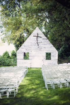 an outdoor ceremony set up with white chairs and a crucifix on the wall