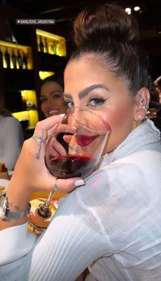 a woman holding a glass of wine in front of her face and smiling at the camera