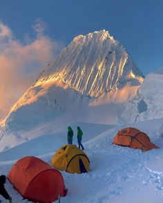 three tents pitched up in the snow with mountains in the back ground and people standing on top of them