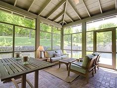 an enclosed patio with seating and table in the middle of it, surrounded by large windows