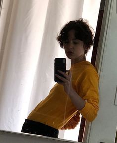 a woman is taking a selfie in the mirror with her cell phone while wearing a yellow sweater