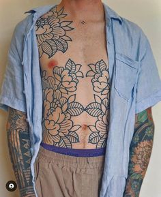 a man with tattoos on his chest and arms is standing in front of a white wall