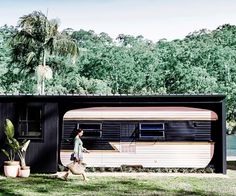 a woman walking past a trailer parked in front of a forest filled with palm trees