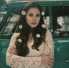 a woman standing in front of a green truck with white flowers on her long hair