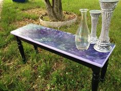 three glass vases sitting on top of a purple table in the grass next to a tree