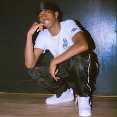 a young man sitting on the floor with his hand to his mouth and wearing white sneakers