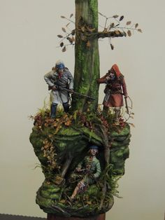 two figurines are standing on top of a moss covered tree trunk with leaves and branches