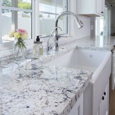 a kitchen sink sitting under a window next to a counter top with soap dispenser