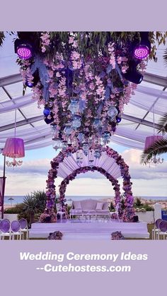 an outdoor wedding setup with purple flowers and chandelier hanging from the ceiling, overlooking the ocean