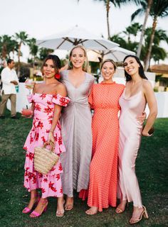 three beautiful women standing next to each other in front of palm trees and umbrellas