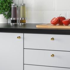 two tomatoes sitting on top of a wooden cutting board next to a potted plant