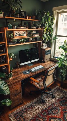 a desk with a computer on top of it in front of a window filled with potted plants