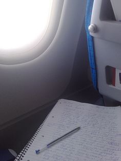 an airplane seat with a notepad and pen on top of it next to a window