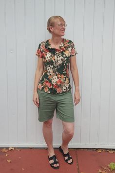 a woman standing in front of a white wall wearing green shorts and a floral shirt