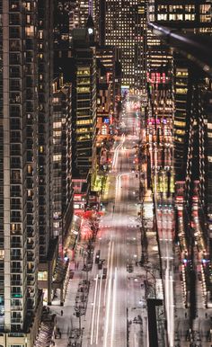 an aerial view of a city street at night with cars driving on the road and tall buildings in the background