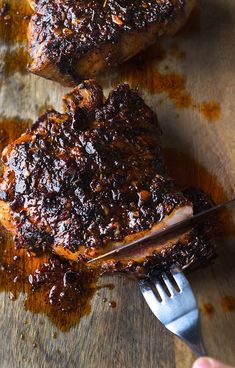 two pieces of meat sitting on top of a wooden cutting board next to a fork