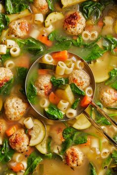 a ladle full of soup with meatballs, spinach and carrots in it