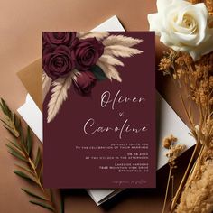 a wedding card with flowers on it next to some dried plants and other things in the background