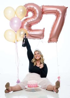 a woman sitting on the floor with balloons and a cake