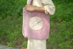 a woman carrying a pink bag with flowers on it in front of green grass and bushes