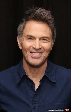 a close up of a person wearing a blue shirt and smiling at the camera with a black background