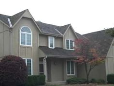 two story house with brown shingles and trees in the front yard on an overcast day