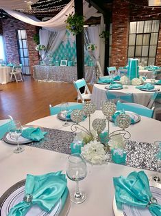 the tables are set with silver and aqua blue napkins, place settings, and centerpieces