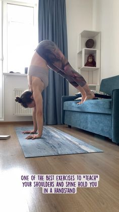 a woman doing a handstand on a yoga mat in front of a blue couch