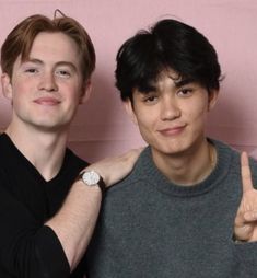 two young men standing next to each other giving the peace sign with their fingers in front of them