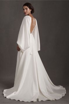 a woman in a white wedding dress with an open back and cape on her shoulder